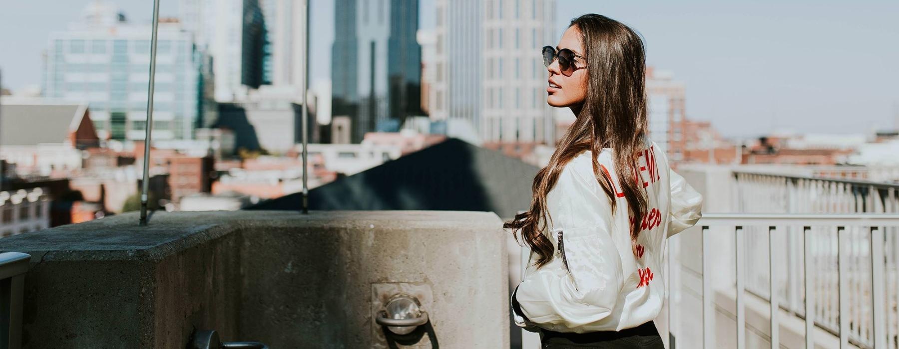 woman with sunglasses stands on a rooftop overlooking the city