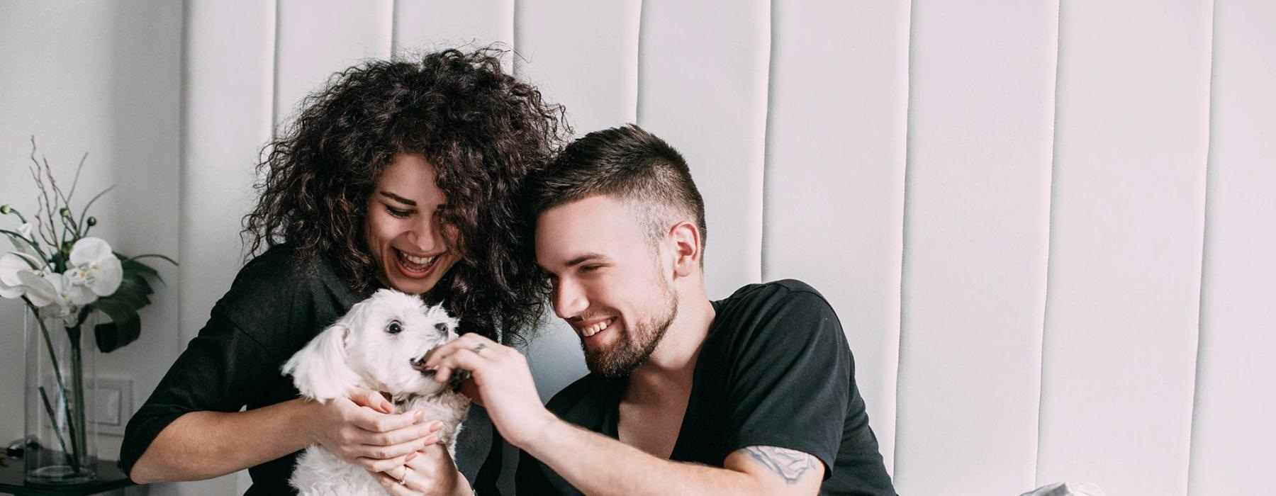 a man and woman sitting on a bed playing with a dog